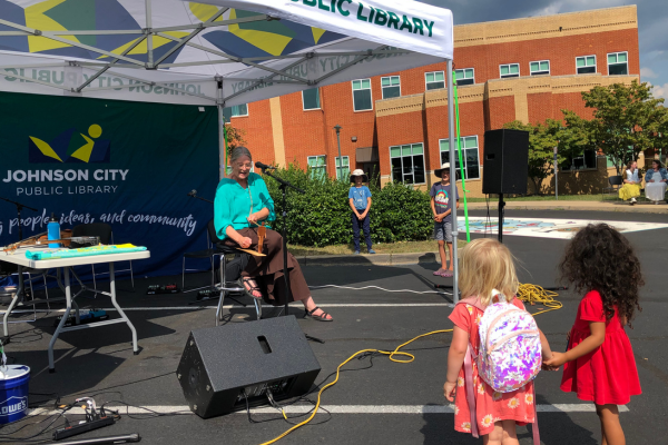 Storyteller Jennifer Armstrong at Public LIbrary event, sitting on a stool talking to two little girls